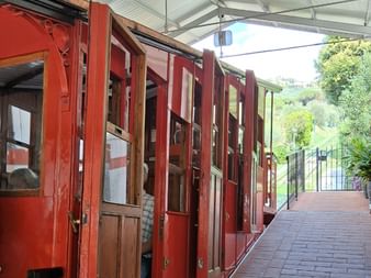 Rote hölzerne Standseilbahn mit offenen Fenstern an einer überdachten Bahnsteig in der Toskana, mit grünen Hügeln im Hintergrund.