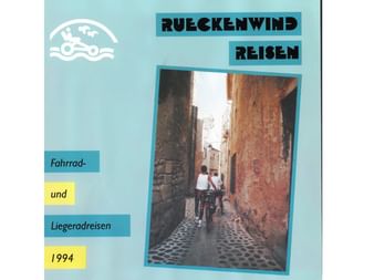 Titelseite des Rückenwind Radreisen-Katalogs 1994 mit Radfahrer in enger Kopfsteinpflastergasse zwischen alten Steinmauern.