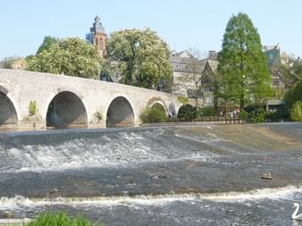 Steinbrücke mit vier Bögen über die Lahn in Wetzlar. Ein Wehr erzeugt fließendes Wasser, ein weißer Schwan ist sichtbar. Historische Gebäude und Kirchturm im Hintergrund.