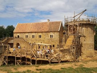 Mittelalterliche Burg im Bau in Burgund mit Holzgerüsten um einen Steinturm und Hauptgebäude. Besucher auf Holzplattformen.