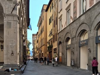 Fußgängerstraße in der Toskana mit mittelalterlichen Steingebäuden, Bogenfassaden und bunten mehrstöckigen Häusern. Menschen gehen auf Steinpflaster.