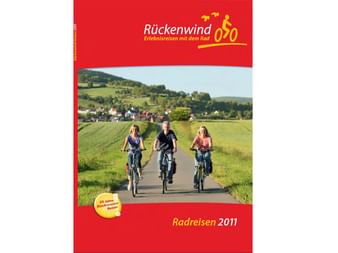 Titelbild des Rückenwind Radreisen Katalogs 2011 mit drei Radfahrern auf einer Landstraße vor grünen Feldern und einem Dorf.