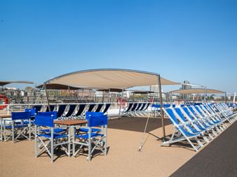 Sun deck of MS Lisabelle with blue and white striped lounge chairs arranged under beige awnings, blue director's chairs and tables on wooden deck.