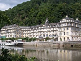 Historisches Kurhaus in Bad Ems mit barocker Architektur, das sich in der Lahn spiegelt. Ausflugsboote liegen an der Uferpromenade.