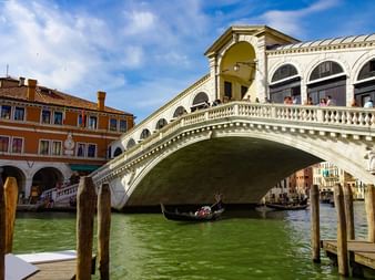 Die berühmte weiße Rialtobrücke überspannt den grünen Canal Grande in Venedig mit Gondeln darunter und historischen Gebäuden an beiden Seiten.