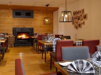 Gemütliches Restaurant mit gedeckten Tischen, rot-grauen Polsterstühlen, Holzboden, brennendem Kamin und Pendelleuchten im Landhotel Schnuck.