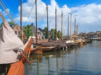Traditionelle hölzerne Segelboote im Hafen von Spakenburg am IJsselmeer, mit historischen Häusern entlang der Uferpromenade unter blauem Himmel.