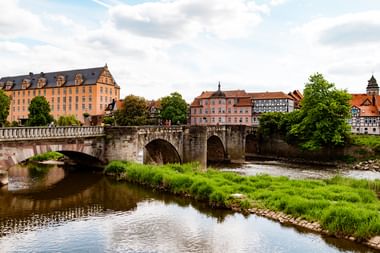 Steinbrücke mit drei Bögen über einen Fluss in Hann. Münden. Historische Gebäude mit roten Dächern säumen das Flussufer unter bewölktem Himmel.
