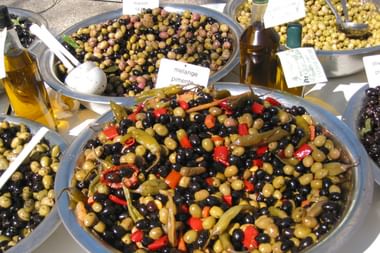 Marktstand mit gemischten Oliven in Schalen mit Paprika in der Provence. Flaschen mit Olivenöl sichtbar. Grüne, schwarze und marinierte Oliven.