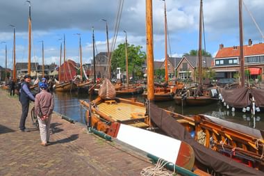 Traditionelle Holzsegelboote mit hohen Masten im Hafen von Spakenburg. Menschen gehen entlang der Kopfsteinpflasterkai mit holländischen Häusern im Hintergrund.