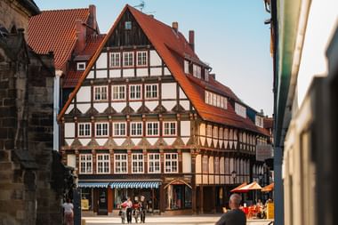 Traditionelle Fachwerkhäuser mit roten Ziegeldächern säumen einen historischen Platz in Hameln. Menschen gehen über das Kopfsteinpflaster.