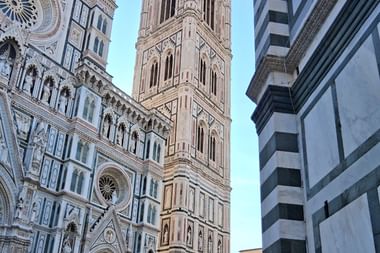 Verzierte Marmorfassade des Florentiner Doms mit geometrischen Mustern und Giottos Campanile vor blauem Himmel in der Toskana, Italien.