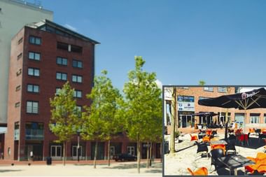 Rotes Backsteingebäude des Fehn City Hotels in Stadskanaal mit Außenterrasse. Modernes mehrstöckiges Hotel mit jungen Bäumen.