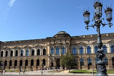 Historisches Semperoper-Gebäude in Dresden mit verzierter Fassade und Bogenfenstern. Eine verzierte Straßenlaterne steht im Vordergrund.