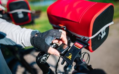 Nahaufnahme der Hände eines Radfahrers am Lenker mit roten Packtaschen am Fahrrad während einer Radtour an der Weser.