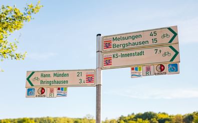 Radweg-Wegweiser mit Entfernungen zu deutschen Städten: Hann. Münden 21km, Ihringshausen 34km, Melsungen 45km, Bergshausen 15km.