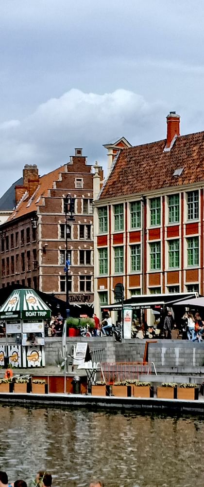 Reihe bunter mittelalterlicher Gildenhäuser mit Treppengiebeln entlang eines Kanals in Brügge, Belgien. Touristen versammeln sich auf Uferterrasse.