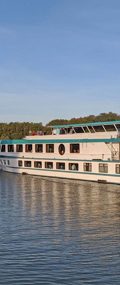 MS Switzerland river cruise ship with white hull and green trim sailing on calm river, surrounded by trees under blue sky.