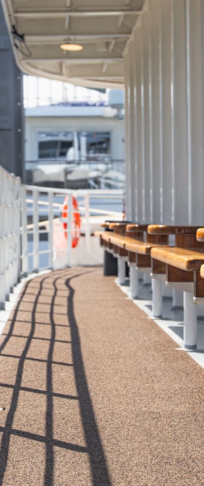 Ship deck of MS Lisabelle with orange life preserver in foreground, wooden benches along white railing, and covered walkway overhead.