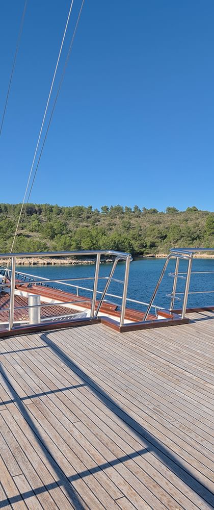 Bugdeck der MY Magellan mit Holzplanken und Metallgeländer, Blick auf blaues Wasser und grüne kroatische Küste unter klarem Himmel.