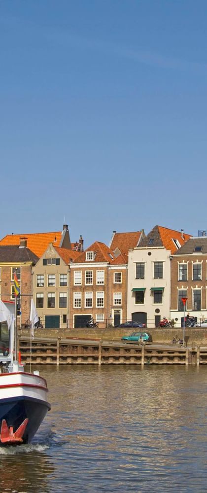 Weißes und blaues Fahrgastschiff auf Fluss mit historischer Deventer Skyline. Bunte Gebäude und hoher Kirchturm unter blauem Himmel.