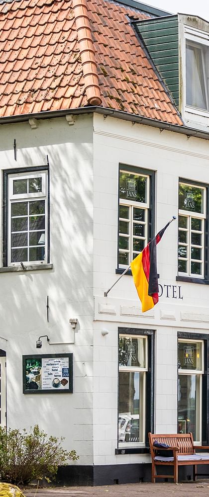 Weißes zweistöckiges Hotelgebäude mit rotem Ziegeldach und Dachgauben. Mehrere Flaggen, darunter deutsche und niederländische, hängen an der Fassade.