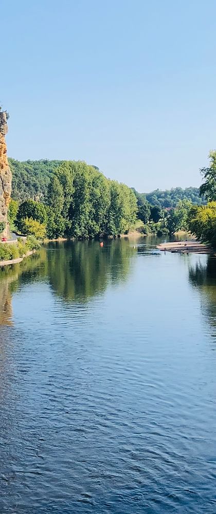 Blick auf die Dordogne mit Kanus auf dem Wasser, Sandstränden an beiden Ufern, üppigen grünen Bäumen und einer Kalksteinklippe links.