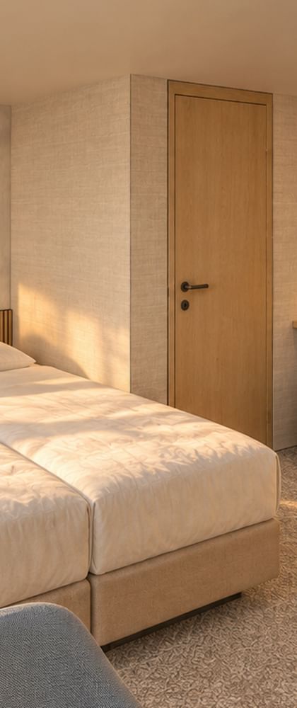 Modern suite on MS Veloria with twin beds, light wood furniture, botanical wall art, and beige carpet. Built-in wardrobes and vanity area visible.