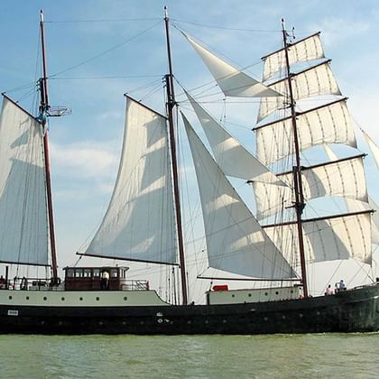 Dreimaster-Segelschiff Simmer fan Fryslan mit weißen Segeln, segelnd auf ruhigem Wasser unter blauem Himmel mit niederländischer Flagge.