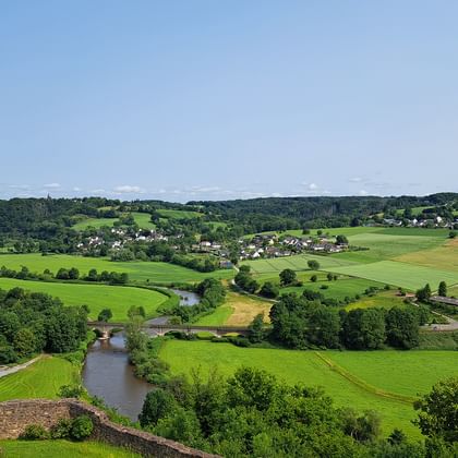 Panoramablick auf einen gewundenen Fluss durch grüne Felder und Ackerland bei Bonn. Ein kleines Dorf liegt im Tal mit Wäldern auf sanften Hügeln.