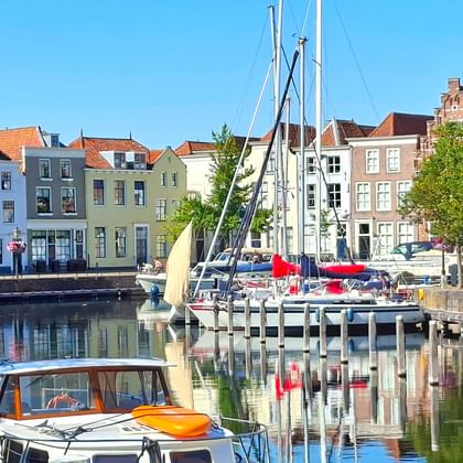 Alter Hafen in Goes mit bunten historischen Häusern, vertäuten Segelbooten und ruhigem Wasser, das die Gebäude unter blauem Himmel spiegelt.