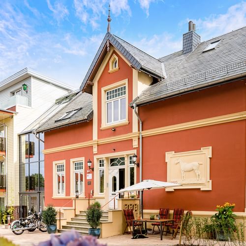 Orangefarbenes historisches Gebäude mit cremefarbenen Verzierungen und grauem Dach, Parkhotel Jever. Modernes weißes Hotelgebäude dahinter.