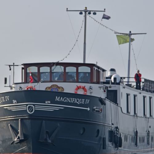 MS Magnifique IV Flusskreuzfahrtschiff auf offenem Wasser. Das Schiff hat einen dunklen Rumpf und weißen Aufbau mit großen Fenstern.