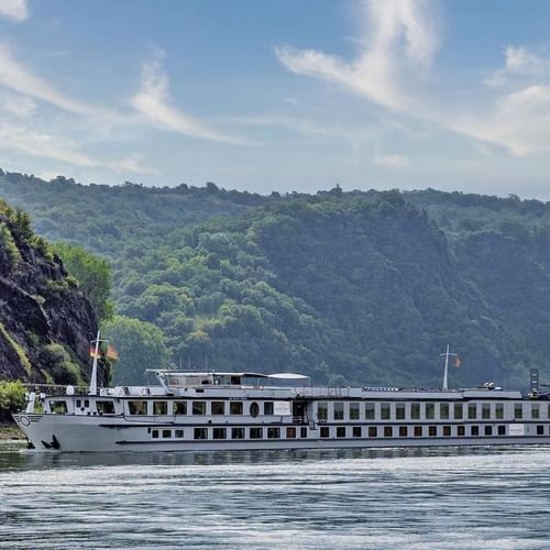 MS Veloria river cruise ship sailing on calm water between steep rocky cliffs covered with green vegetation under a blue sky.