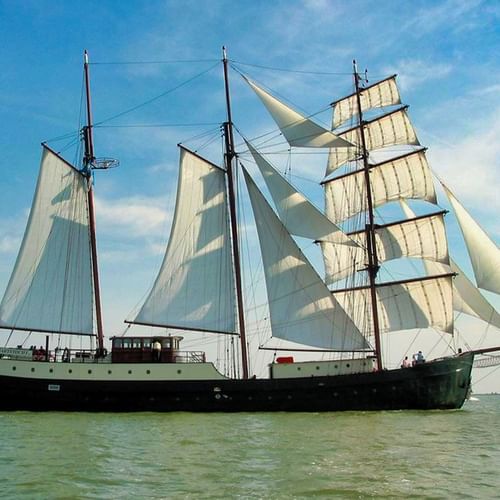 Traditionelles dreimastiges Segelschiff Simmer Fan Fryslân mit weißen Segeln auf ruhigem Wasser unter blauem Himmel mit Wolken.