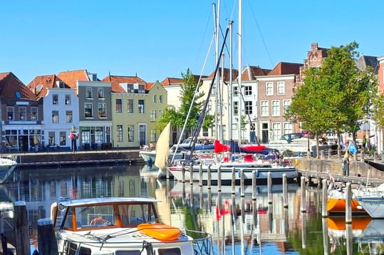 Alter Hafen in Goes mit bunten historischen Häusern, vertäuten Segelbooten und ruhigem Wasser, das die Gebäude unter blauem Himmel spiegelt.