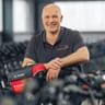 Knut Wulfestieg in dark polo shirt leaning on bicycle handlebar in workshop with rows of bikes in background.