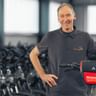 Thomas Brandhorst in dark polo shirt standing with a Vaude bicycle with red Rückenwind bag in a bike storage facility.