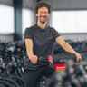 Basti Stüdemann in schwarzem Poloshirt steht mit Fahrrad in großer Lagerhalle voller Fahrradreihen.