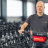 Michael Schubert in grauem Poloshirt steht mit Fahrrad vor Reihen schwarzer Fahrräder in einer hellen Lagerhalle.