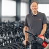Achim Wendland im grauen Poloshirt steht mit Fahrrad in großer Lagerhalle mit Fahrradreihen im Hintergrund.