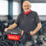 Juergen Bunge mit Brille und rotem Schal steht mit einem Fahrrad in einer großen Lagerhalle voller Fahrradreihen.